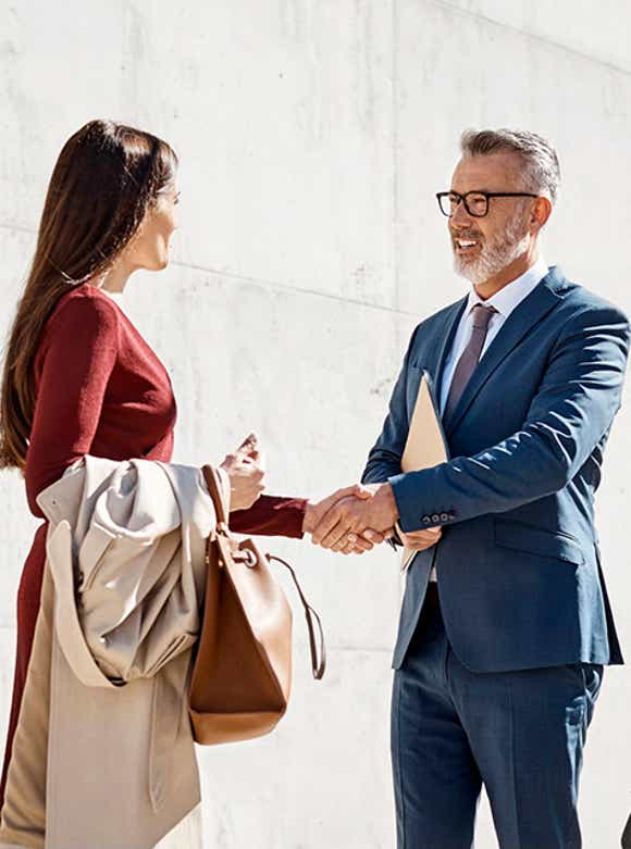 stylish male and female business professionals shaking hands outside a modern office building on a sunny day symbolizing richardson's deep alliance partnerships in the sales improvement industry