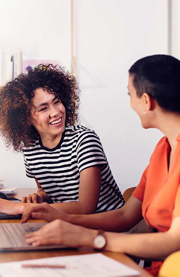 a young female sales professional and her manager sitting at a desk with a computer in an airy office working on their channel partner management plan using the skills they learned in richardson's channel partner management training program