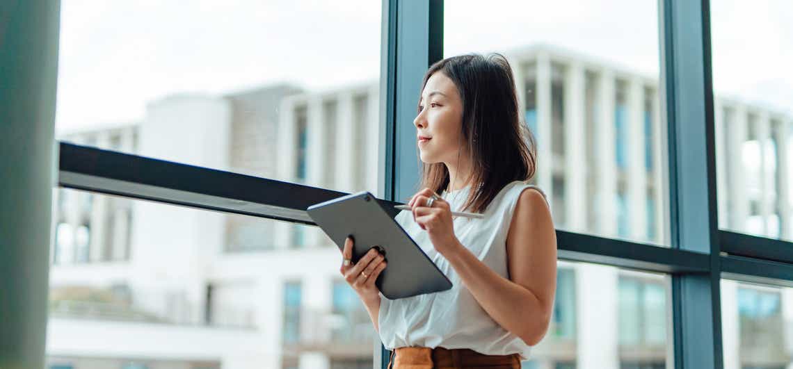 young account manager using an account planning tool on a tablet looking out the window smiling because the tool is helping her grow her revenue.